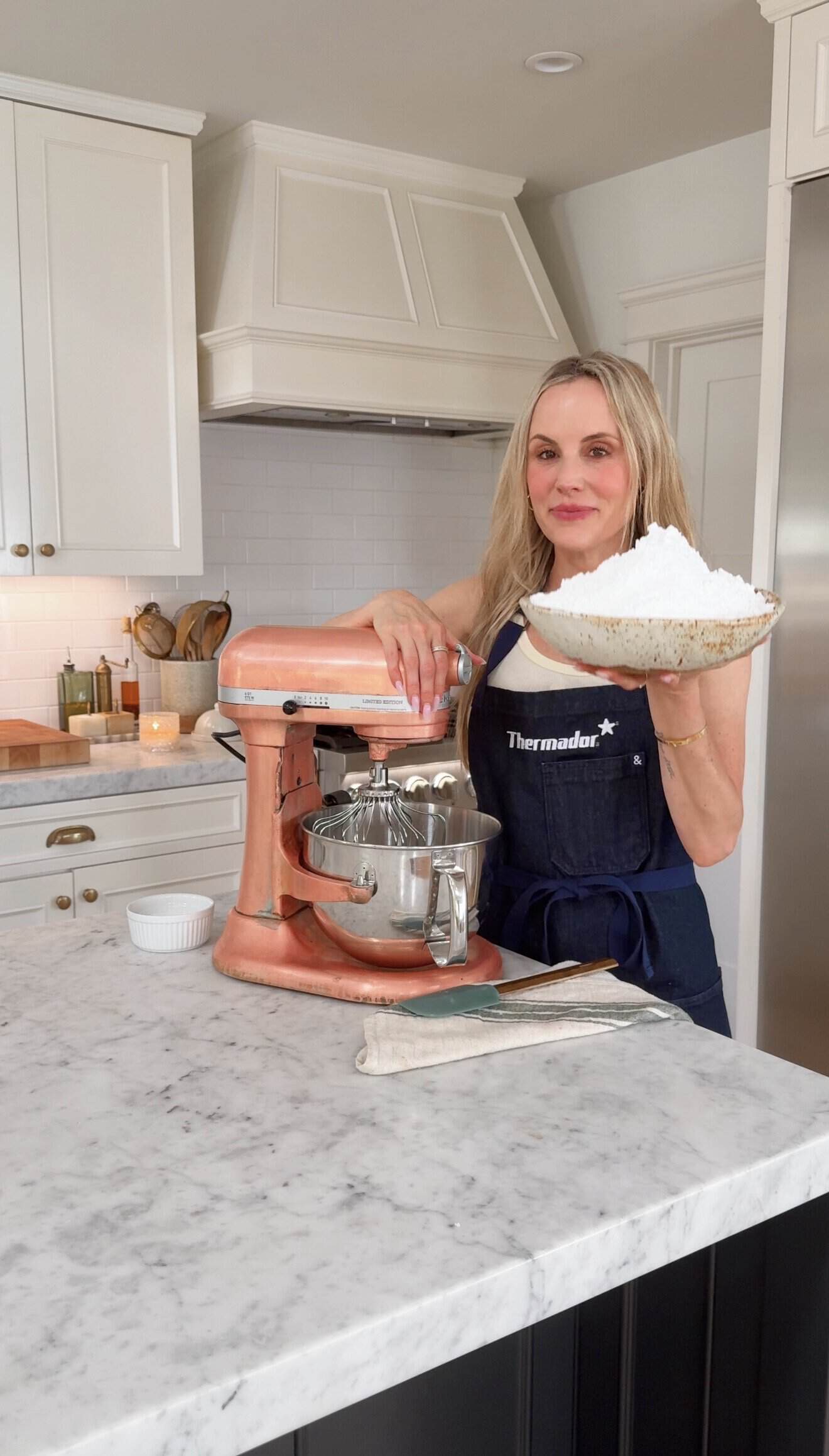 Jessie Daye holding a bowl of flour in a modern kitchen with stand mixer.