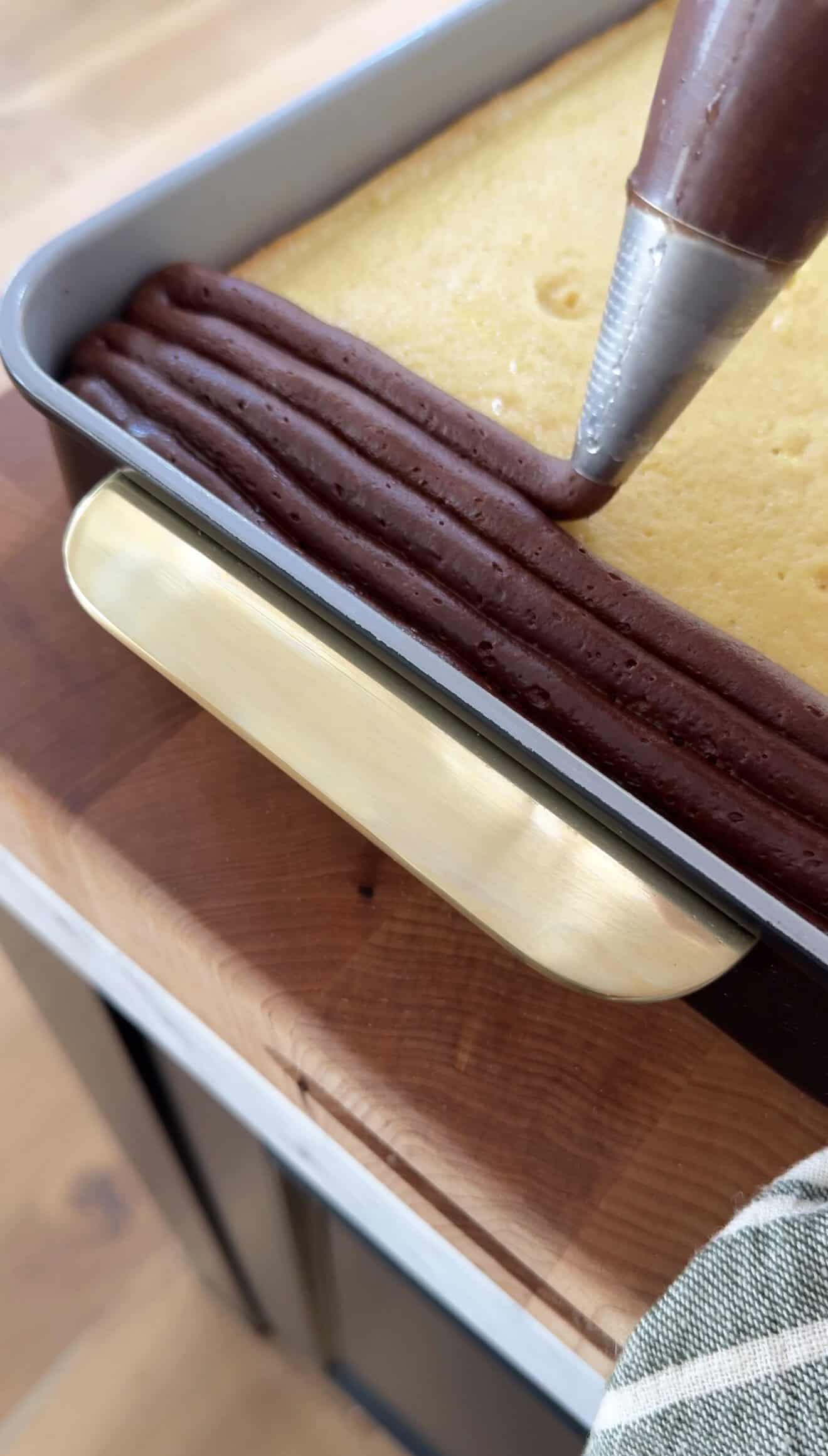Applying chocolate frosting to yellow cake in a baking pan.