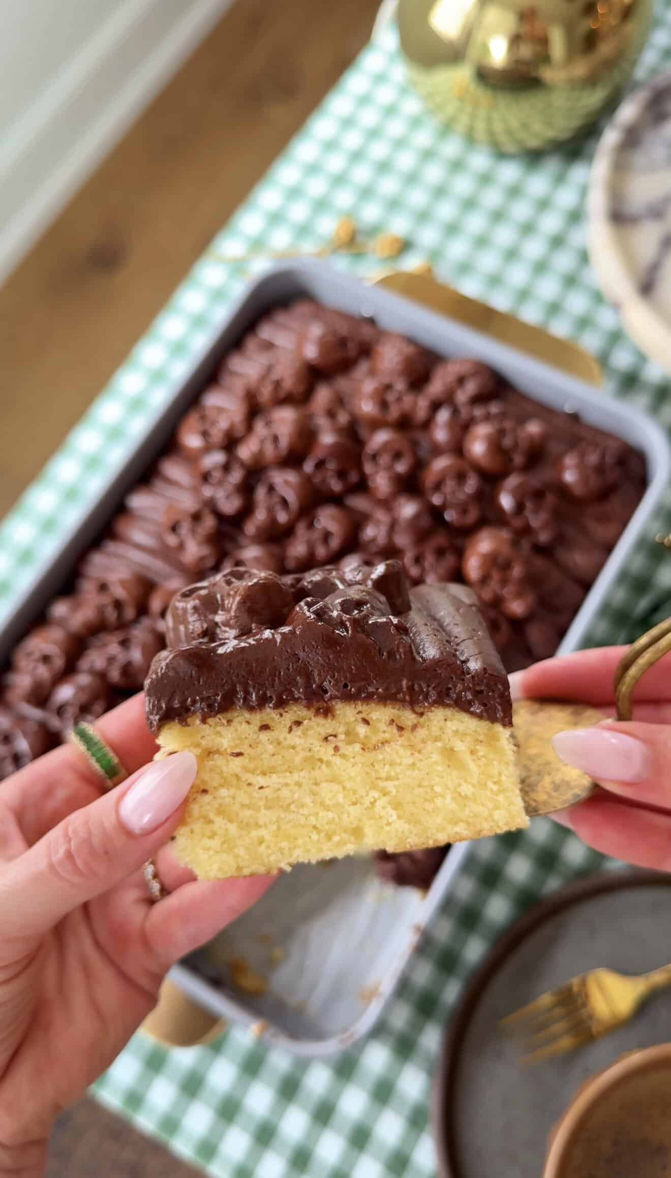 Slice of yellow cake with chocolate frosting held over a baking dish.