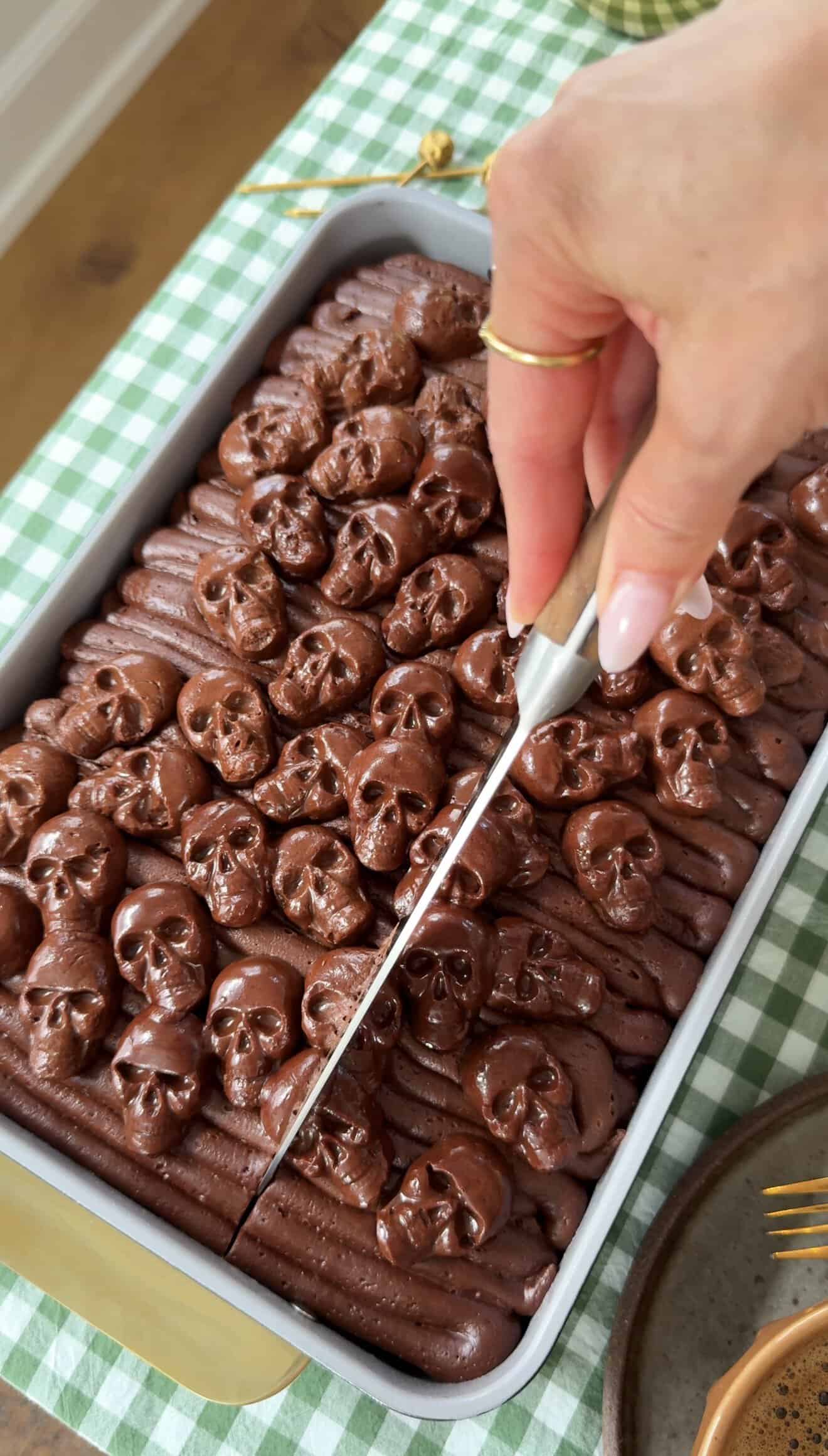 Hand cutting chocolate skulls in a baking dish for Halloween treats.