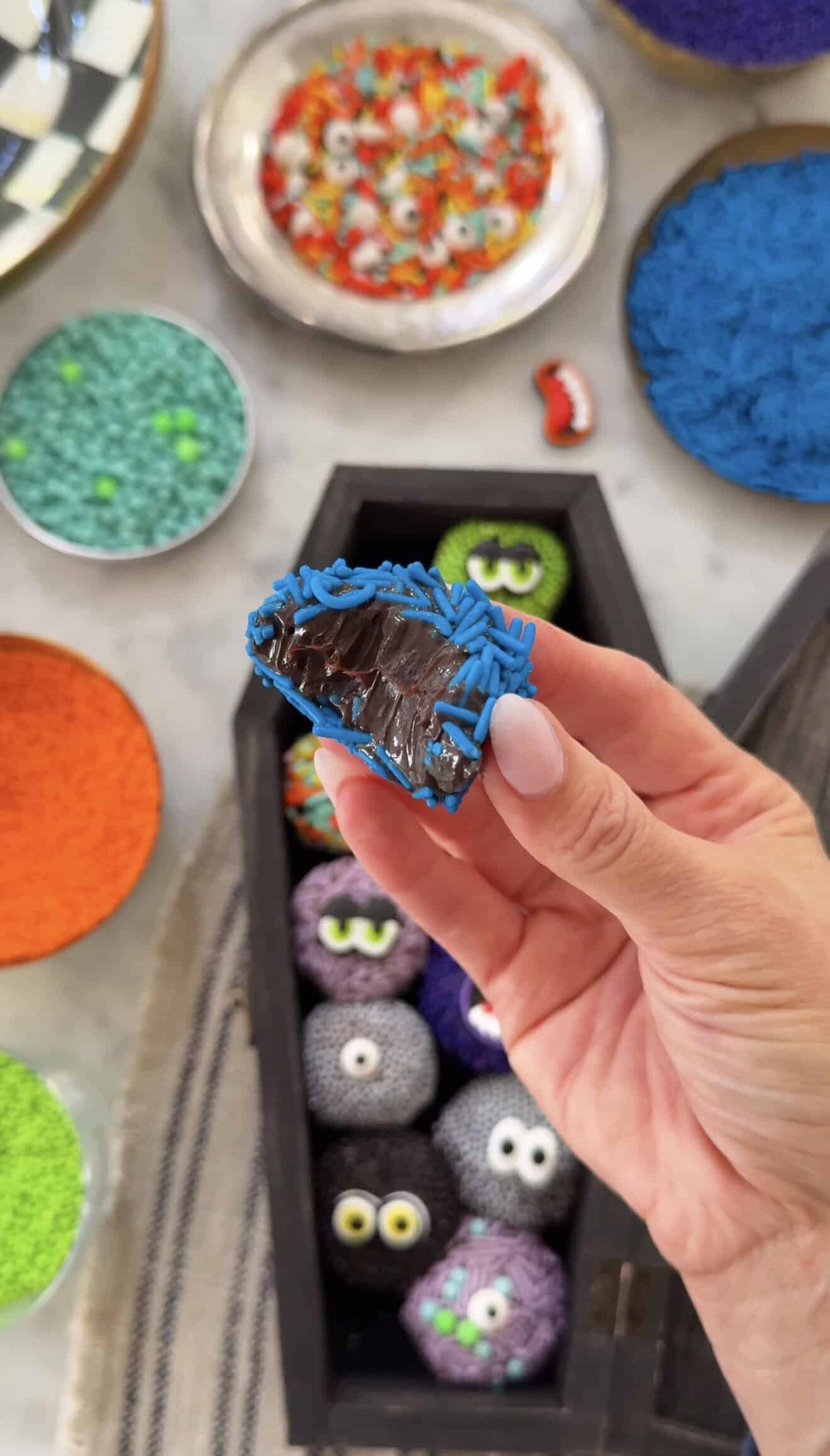 Hand holding a spooky monster brigadeiro with colorful sprinkles and decorations.